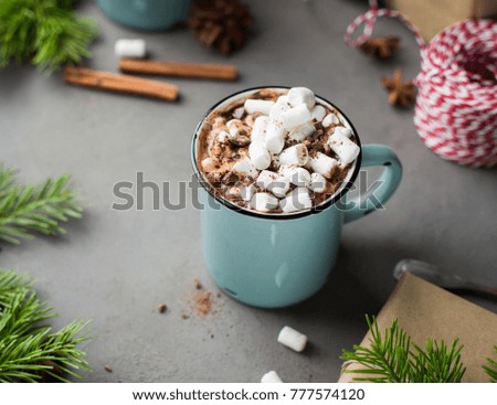Mug of hot chocolate with marshmallow and cinnamon on a gray concrete background with a Christmas tree, gifts. and red-white string (twine). Winter xmas holidays concept. Festive mood.