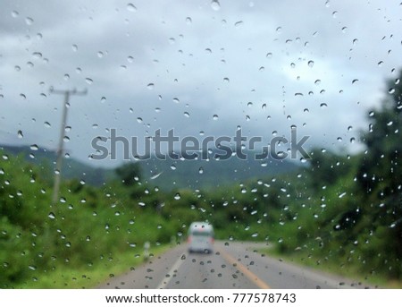 shoot picture inside car for image of water drop on  car 's glass window while on the way in countryside road with mountain , sky moody and other car outside blur background.concept water drop     