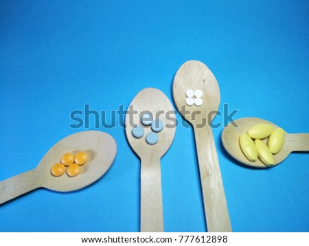 Colorful pills in four wooden spoon on a blue paper texture background  