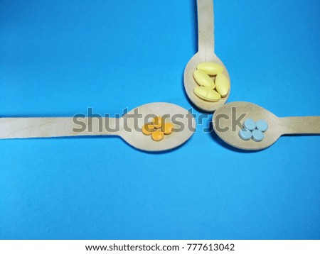 Colorful pills in 3 wooden spoons on a blue paper texture background  