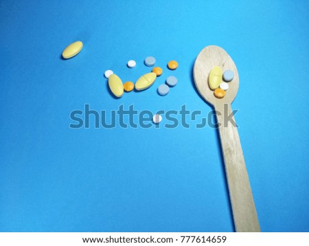Colorful pills in wooden spoon on a blue paper texture background  