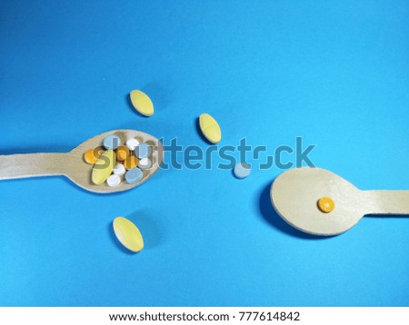 Colorful pills in two wooden spoon on a blue paper texture background  