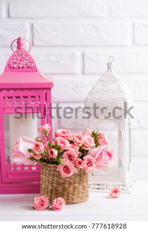 Pink roses flowers and decorative pink and white lanterns against  white brick wall. Floral still life.  Selective focus. Place for text. Vertical image.