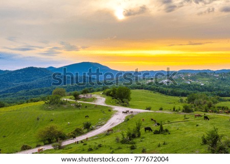 Sunset behind the clouds over the mountainous countryside, the road is in the green pastures. Rural evening spring landscape in Sochi, Russia.
