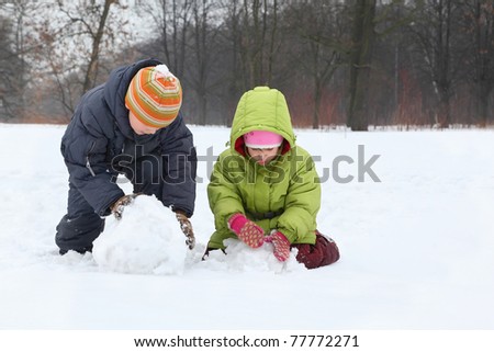 Brother and sister sculpt snowman in street in winter