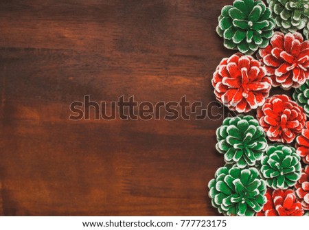 Christmas brown wooden background decorated with real pine cones painted in red and green colors. With copyspace in left side. Horizontal color photography.