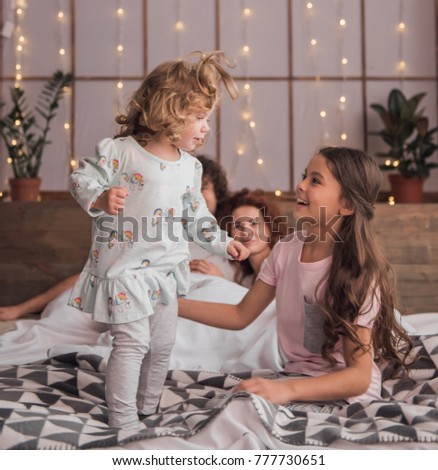It's Christmas time! Happy parents and their daughters are opening the presents and smiling while spending time together in bed at home