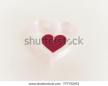 Small red heart in bigger pink ribbon heart with white background.