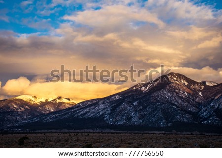 Golden sunset view of Taos , New Mexico Mountains outside of the city as clouds roll in and the sun paints a golden picture as it sets winter scene and winter shrubs