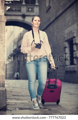 Blonde girl is walking around the city with camera. 