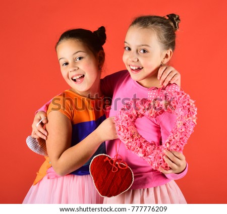 Children celebrate Valentines day. Sisters with paper decorative furry and soft hearts. Girls with cheerful faces hug on red background. Holiday and love concept.
