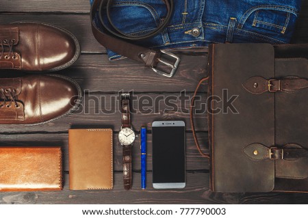 Top view, men's fashion personal belongings and accessories with space on a dark wooden background. Leather bag, shoes, watch, jeans, belt.