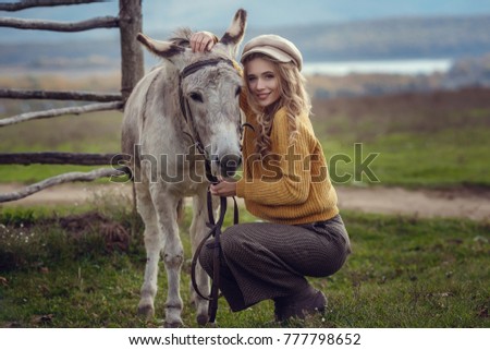 A girl with blond hair in fashionable clothes in the style of Provence hugs a cute donkey