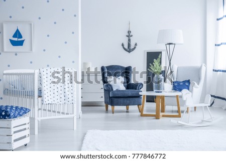 White kid's bed in bright room with armchairs, lamp and vase on table with marine decorations