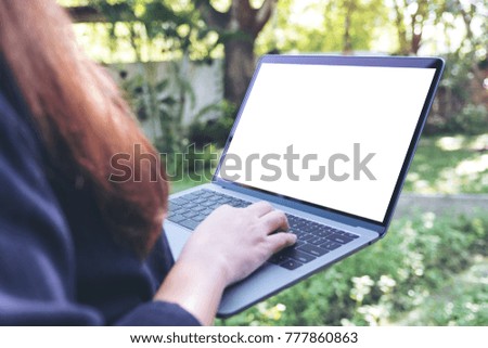 Mockup image of business woman holding and typing on laptop with blank white screen , standing at outdoor with nature background