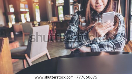 Closeup image of a beautiful Asian woman holding , using and looking at smart phone in modern cafe