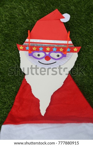 Santa Claus looks so cute with glasses,that made form papers stickers Santa hat and draw decoration for Christmas,top view on grass background 