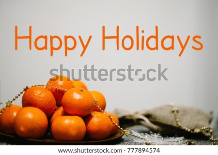 Text Happy Holidays. Tangerines in plate and rustic stylish sack on gray knitted background. space for text, design. Greeting Festive Card. Merry Christmas Happy New Year's 2018 Celebration Concept.