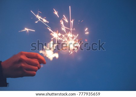 Abstract blur sparklers for celebration background,Motion blurred by wind  woman hand holding burning Christmas sparkle on nature blue sky and bokeh background.Winter vintage film grain filter style.