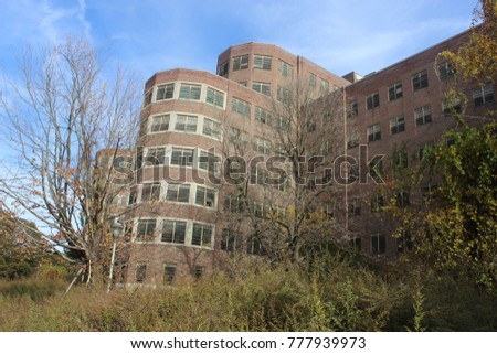 Exterior of boarded up and abandoned brick asylum hospital building with broken windows
