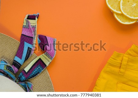 Travel and tourism concept. A bright orange background with beach shorts and a straw hat with a ribbon, top view. Space for a text or product display.