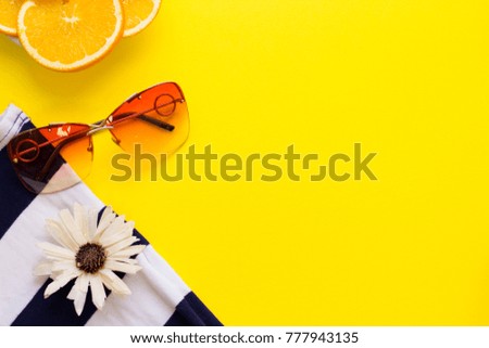 Beach concept background. Sunglasses, slices of orange and a striped beach shirt on a bright yellow background, top view. Space for a text or product display.