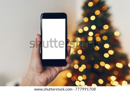hand holding phone with empty screen on background of beautiful christmas tree lights. merry christmas and happy new year concept. space for text. seasonal greetings, happy holidays