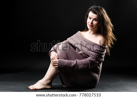 Photo of a sensitive woman in knitted dress sitting on the floor on a dark background