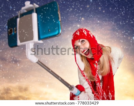 A young woman in a knitted hat scarf and mittens takes pictures of herself on the phone in a winter forest