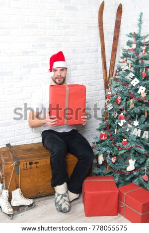 Macho in red hat hold wrapped present. Gift giving and exchange. Man santa with boxes at christmas tree. Boxing day concept. Winter holidays, fun, sports