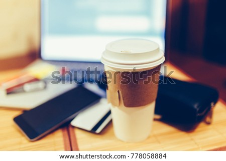 White paper Cup with burning coffee on the background of laptop and smartphone. Scattered Bank cards and a black purse. Work on the go. Toned photo.
