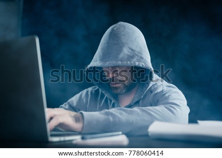 A computer hacker is typing on a laptop in a smoky room. Dark background