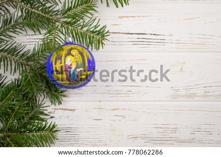 a branch of spruce and a Christmas tree toy with the image of biblical characters. white wooden background. christmas background
