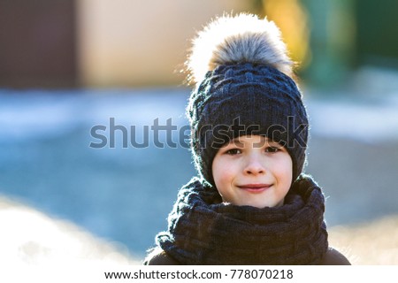 Portrait of child boy in hat and scarf outdoors in sunny winter day