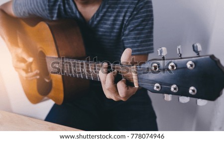 Man wearing a striped shirt playing guitar in his room with romantic atmosphere full of symphonic music.