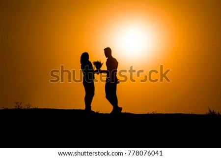 Silhouette of a couple sharing a romantic moment at suns, young man gives flowers to his lover, young lover silhouette at sunset