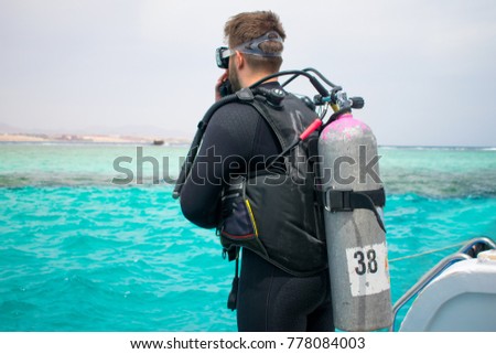 A diver in diving gear is preparing to dive. a man in a wet suit, with an aqualung,mask and a balloon, jumps into the water. scuba. scuba diving. snorkeling. hobby. azure sea.  Royalty-Free Stock Photo #778084003