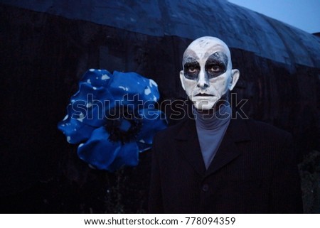 A man in a terrible make-up of an alien. An alien on a black planet with a blue flower. A dull character at night.