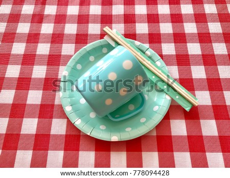 Closeup light green polka dot paper plate and cup with wooden chopsticks on red & white check background. The concept of food display,party accessories, picnic utensils.Top view with Selective focus.