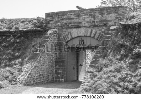 A black and white photograph of the stone entrance and open wooden gate of Fort Wellington, used in the War of 1812, in historic Prescott, Ontario, Canada.