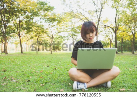 Young asian woman's legs on the green grass with open laptop. Girl's hands on keyboard. Distance learning concept. Happy hipster young asian woman working on laptop in park. Student studying outdoors.