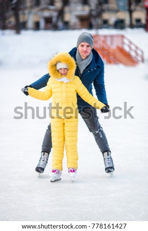 Young dad and adorable little girl have fun on skating rink