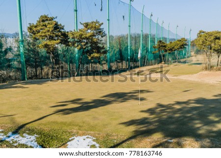 Putting green on a bright sunny day with shadows of trees and flag falling across the green and a patch of snow in the foreground