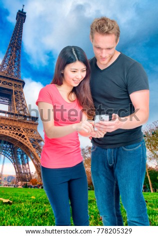Asian girl and caucasian boy happy reviewing Paris pictures near Eiffel Tower.