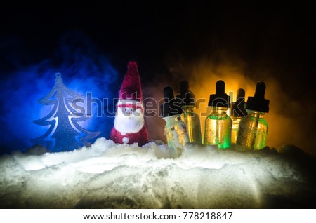 Electronic cigarette with vape liquids and christmas decorations on bokeh lights background with New Year atributes or symbols. Selective focus