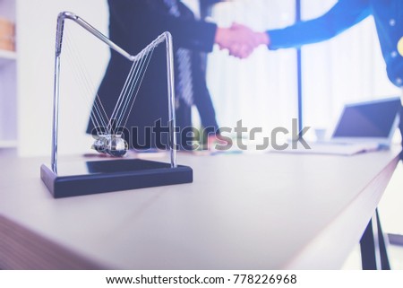 Newton's cradle ball and business partners shaking hands as background. business effect concept