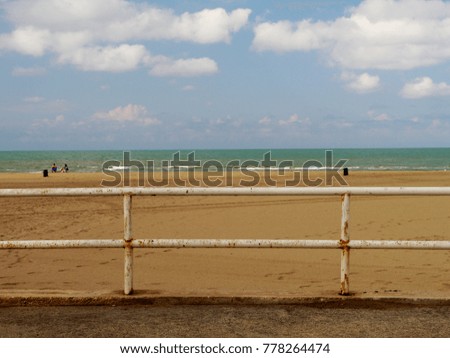 Minimalist picture of a rusty white steel railing at empty sand beach with sea and cloudy sky in the background