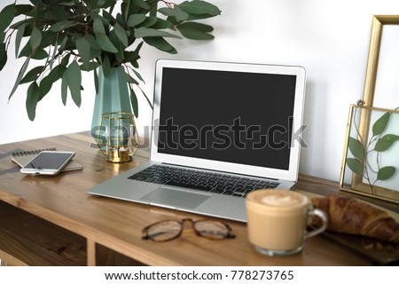 Interior of a cozy feminine home office with laptop mock-up, eucalyptus plant in vase, glasses, coffee cup, phone and frames. Styled blogger's workplace