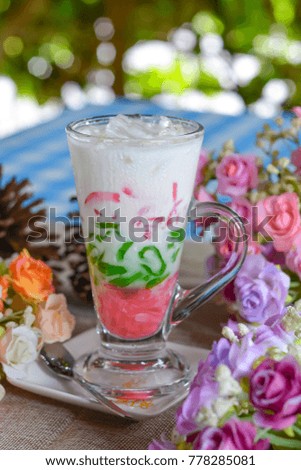 Green and pink Cendol in glass with coconut milk.