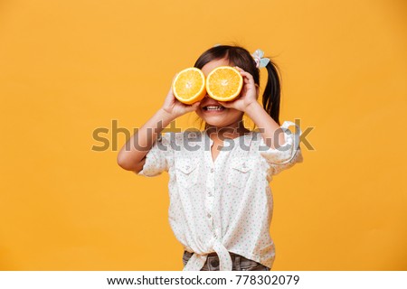 Photo of little girl child standing isolated over yellow background. Covering eyes with orange. Royalty-Free Stock Photo #778302079